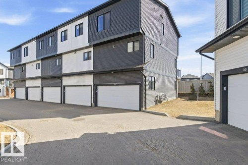 The property features a modern exterior with dark gray and white siding, individual garages, and a paved driveway - 49 850 Secord Boulevard, Edmonton, AB - Outdoor With Exterior