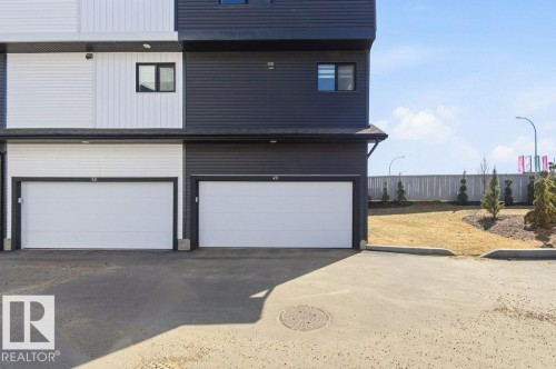The property features a modern exterior with dark and light-colored siding, a garage with a white door, and a paved driveway - 49 850 Secord Boulevard, Edmonton, AB - Outdoor