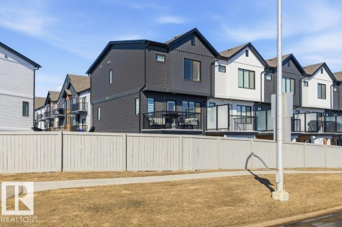 The property features modern exterior design with contrasting dark and light siding, individual balconies with glass railings, and a private fenced yard - 49 850 Secord Boulevard, Edmonton, AB - Outdoor
