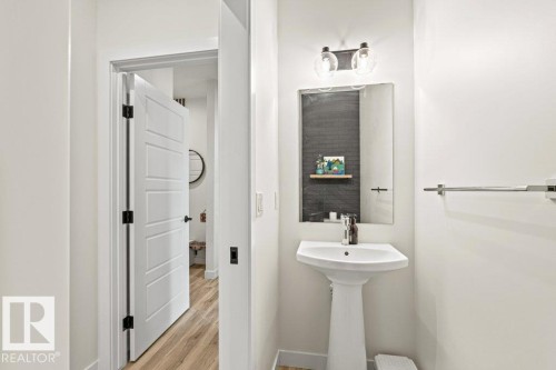This powder room features a pedestal sink with a single-handle faucet, a mirror with a dark frame, and a two-bulb vanity light fixture - 21003 131 Avenue, Edmonton, AB - Indoor Photo Showing Bathroom