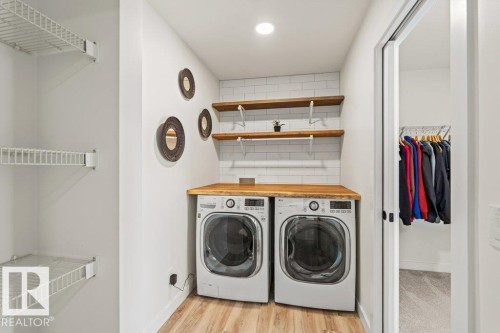Laundry area featuring a side-by-side washer and dryer, a wood countertop, open shelving, and a tiled backsplash - 21003 131 Avenue, Edmonton, AB - Indoor Photo Showing Laundry Room