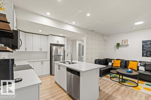The open-concept living area features a kitchen with white cabinetry, a white subway tile backsplash, stainless steel appliances, and an island with a sink - 21003 131 Avenue, Edmonton, AB - Indoor Photo Showing Kitchen With Double Sink With Upgraded Kitchen