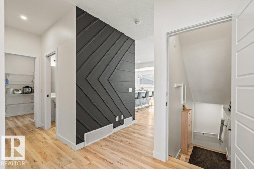 Inviting hallway featuring hardwood floors, a distinctive dark accent wall with a geometric pattern, and a glimpse of the kitchen with a breakfast bar - 21003 131 Avenue, Edmonton, AB - Indoor Photo Showing Other Room