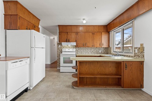 The kitchen features wood cabinetry, white appliances, and a tiled backsplash - 8608 156 Street, Edmonton, AB - Indoor Photo Showing Kitchen With Double Sink