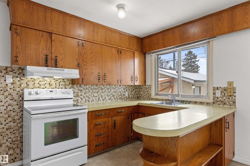The kitchen features wood cabinetry, a mosaic tile backsplash, and a window with outdoor views - 8608 156 Street, Edmonton, AB - Indoor Photo Showing Kitchen