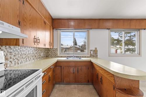 The kitchen features wood cabinetry, a tiled backsplash, and a U-shaped countertop with an integrated breakfast bar - 8608 156 Street, Edmonton, AB - Indoor Photo Showing Kitchen