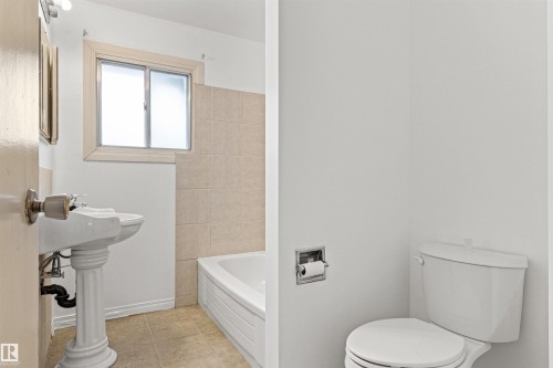 Bathroom featuring a pedestal sink, white bathtub with tiled surround, and a window - 8608 156 Street, Edmonton, AB - Indoor Photo Showing Bathroom
