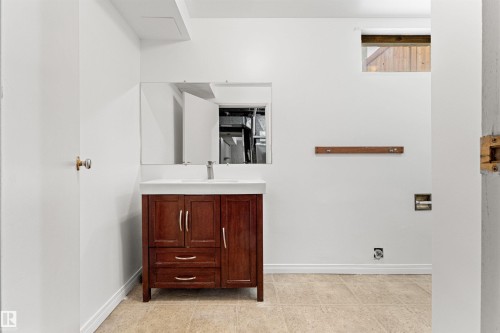 Bathroom featuring a dark wood vanity with a white countertop and an integrated sink, a wall-mounted mirror, and tile flooring - 8608 156 Street, Edmonton, AB - Indoor