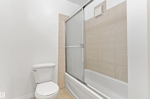 Bathroom featuring a toilet, a bathtub with a sliding glass door, and tiled walls in the shower area - 8608 156 Street, Edmonton, AB - Indoor Photo Showing Bathroom