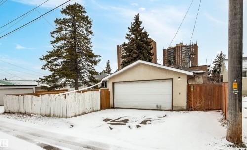 Detached garage with a white garage door, featuring a light-colored exterior and a brown fence - 8608 156 Street, Edmonton, AB - Outdoor