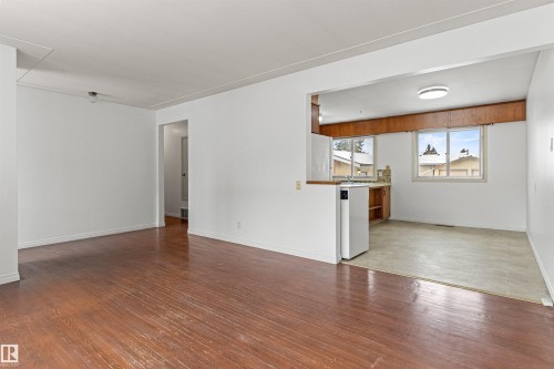 Spacious living area featuring hardwood floors and an open concept view into the kitchen, which includes a window and wood cabinetry - 8608 156 Street, Edmonton, AB - Indoor