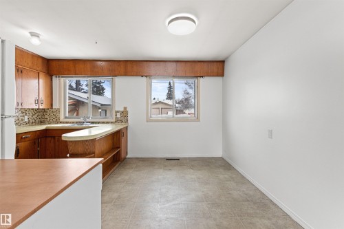 The kitchen features ample wood cabinetry, a tiled backsplash, and two windows providing natural light - 8608 156 Street, Edmonton, AB - Indoor
