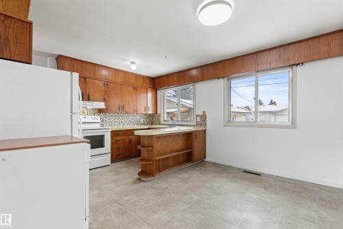 Kitchen featuring wood cabinetry, a mosaic tile backsplash, and two windows providing natural light - 8608 156 Street, Edmonton, AB - Indoor Photo Showing Kitchen