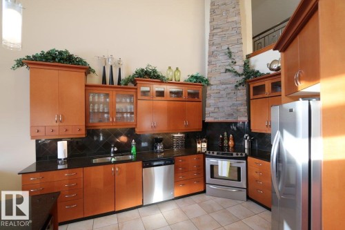 Kitchen with appliances with stainless steel finishes, glass insert cabinets, brown cabinets, light tile patterned flooring, and dark stone countertops - 1402 9707 105 Street, Edmonton, AB - Indoor Photo Showing Kitchen