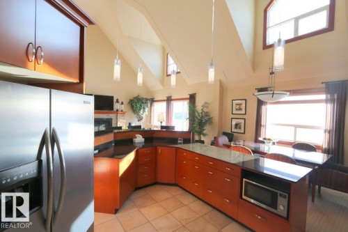 Kitchen with appliances with stainless steel finishes, high vaulted ceiling, hanging light fixtures, dark stone counters, and light tile patterned flooring - 1402 9707 105 Street, Edmonton, AB - Indoor Photo Showing Kitchen