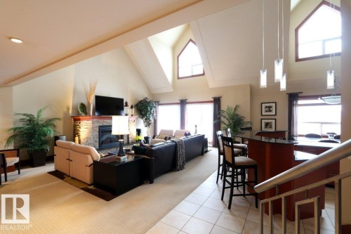 Living area featuring high vaulted ceiling, a stone fireplace, light colored carpet, and light tile patterned floors - 1402 9707 105 Street, Edmonton, AB - Indoor With Fireplace