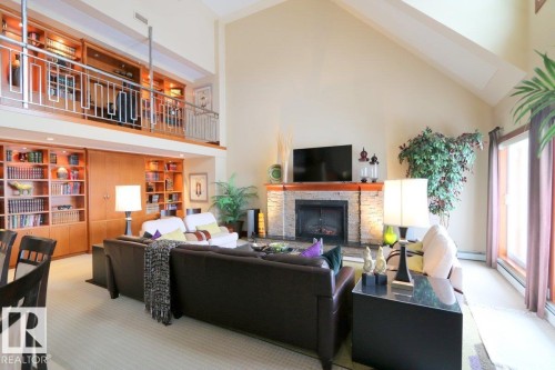 Carpeted living area featuring high vaulted ceiling, a fireplace, built in shelves, and a baseboard heating unit - 1402 9707 105 Street, Edmonton, AB - Indoor With Fireplace