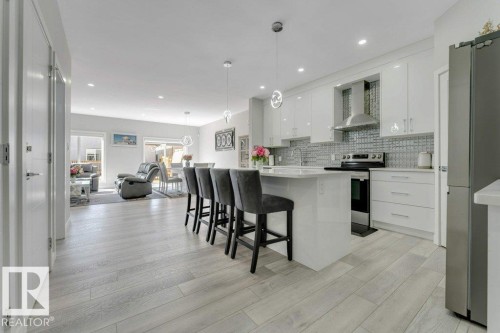 The property features an open-concept living space with light-toned flooring, a kitchen island with seating, white cabinetry, and stainless steel appliances - 452 Roberts Crescent, Leduc, AB - Indoor Photo Showing Kitchen With Upgraded Kitchen