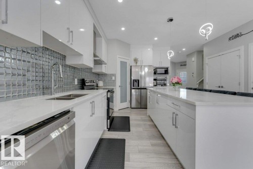 This kitchen features white cabinetry, stainless steel appliances, light-colored countertops, and a full-height tiled backsplash - 452 Roberts Crescent, Leduc, AB - Indoor Photo Showing Kitchen With Double Sink With Upgraded Kitchen