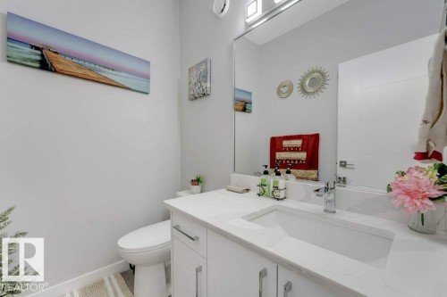 This bathroom features a contemporary vanity with a white countertop and an integrated sink, complemented by a large mirror and modern light fixture - 452 Roberts Crescent, Leduc, AB - Indoor Photo Showing Bathroom