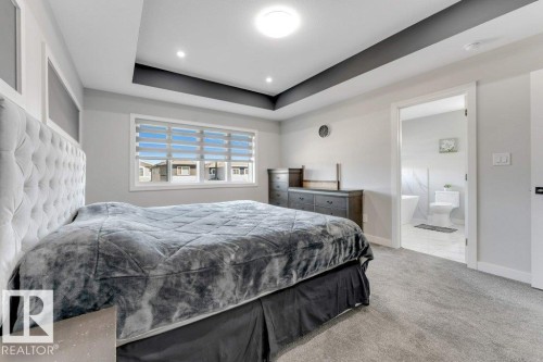 This spacious sleeping area features a tray ceiling with recessed lighting, a large window providing natural light, and carpeting - 452 Roberts Crescent, Leduc, AB - Indoor Photo Showing Bedroom