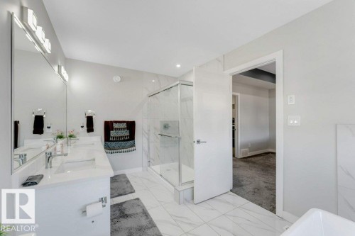 The bathroom features a dual vanity with rectangular sinks and chrome fixtures, a spacious glass-enclosed shower, and a white tiled floor - 452 Roberts Crescent, Leduc, AB - Indoor Photo Showing Bathroom