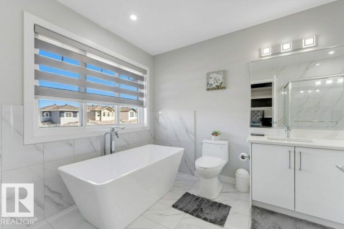 The bathroom features a freestanding bathtub, a vanity with a rectangular sink and mirror, and a window with horizontal blinds - 452 Roberts Crescent, Leduc, AB - Indoor Photo Showing Bathroom