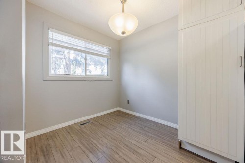 This room features wood-look flooring, a window providing natural light, and a built-in storage unit with paneled doors - 12032 25 Avenue, Edmonton, AB - Indoor Photo Showing Other Room