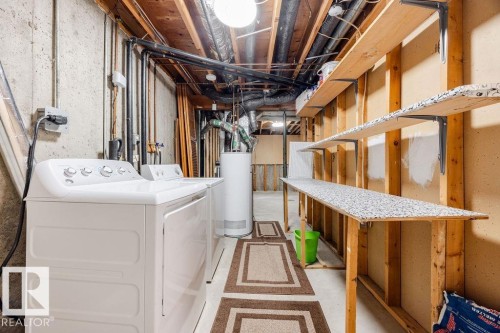 The utility space features a white top-load washing machine and dryer, a water heater, and built-in shelving with patterned tops - 12032 25 Avenue, Edmonton, AB - Indoor Photo Showing Laundry Room