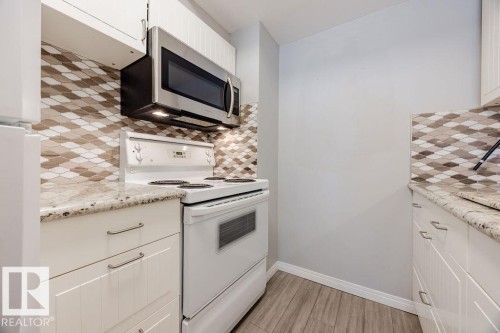 Kitchen featuring white cabinetry, granite countertops, a patterned tile backsplash, and a stainless steel microwave - 12032 25 Avenue, Edmonton, AB - Indoor Photo Showing Kitchen