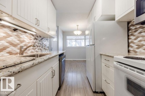 The kitchen features white cabinetry, granite countertops, a stainless steel sink with a modern faucet, and a patterned backsplash - 12032 25 Avenue, Edmonton, AB - Indoor Photo Showing Kitchen With Upgraded Kitchen