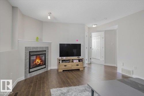 Living area featuring dark hardwood style flooring, light colored walls, a corner fireplace with a tiled surround, and a white interior door - 3119 32 Avenue, Edmonton, AB - Indoor Photo Showing Living Room With Fireplace