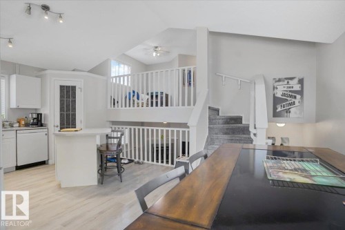Open concept living area featuring light-colored flooring, a kitchen area with white cabinetry, and a dining area with a dark wood table - 3119 32 Avenue, Edmonton, AB - Indoor Photo Showing Other Room