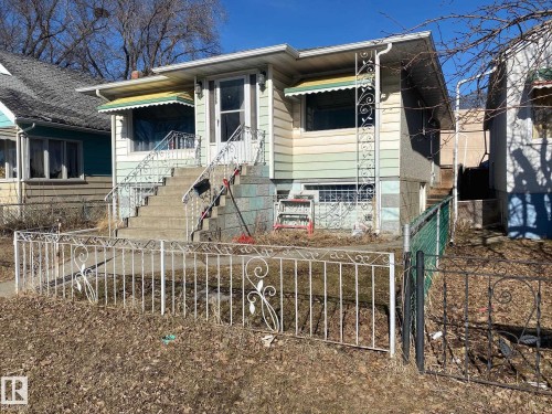 The property features an exterior with light-colored siding, a concrete staircase with white wrought iron railings, and decorative awnings over the front windows - 10965 96 Street Nw, Edmonton, AB - Outdoor