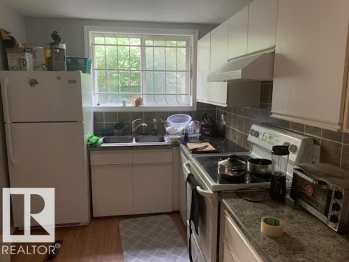 The kitchen features white cabinetry, a double basin sink, and a window with security bars - 10965 96 Street Nw, Edmonton, AB - Indoor Photo Showing Kitchen
