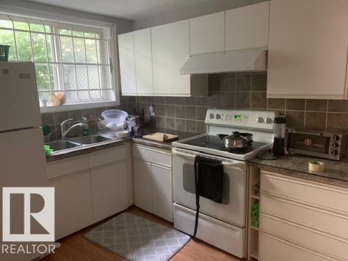 The kitchen features white cabinetry, a double basin sink, and a white electric range - 10965 96 Street Nw, Edmonton, AB - Indoor Photo Showing Kitchen With Double Sink