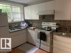 The kitchen features white cabinetry, a double basin sink, and a white electric range - 