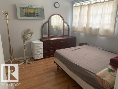 This room features wood-look flooring, light-colored walls, and a window with curtains - 10965 96 Street Nw, Edmonton, AB - Indoor Photo Showing Bedroom