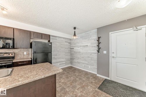 The kitchen and dining area feature dark wood cabinetry, black appliances, and a light-toned countertop - 301 103 Ambleside Drive, Edmonton, AB - Indoor Photo Showing Kitchen