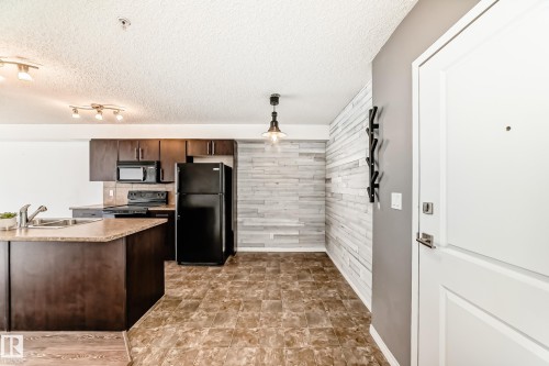The kitchen features dark wood cabinetry, black appliances, and an island with a sink and countertop - 301 103 Ambleside Drive, Edmonton, AB - Indoor Photo Showing Kitchen With Double Sink