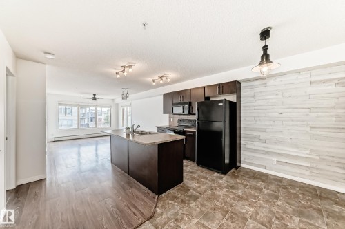 Open-concept living space featuring a kitchen island with a double sink, dark wood cabinetry, and stainless steel appliances - 301 103 Ambleside Drive, Edmonton, AB - Indoor Photo Showing Kitchen