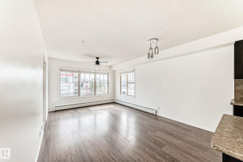 The open concept living area features dark wood-look flooring, white walls, and large windows that provide abundant natural light - 301 103 Ambleside Drive, Edmonton, AB - Indoor Photo Showing Other Room