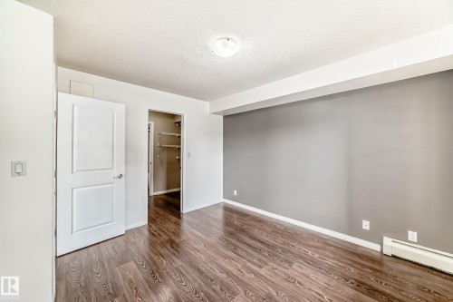 The property features richly toned wood-style flooring, a warm gray accent wall, and a white baseboard heater - 301 103 Ambleside Drive, Edmonton, AB - Indoor Photo Showing Other Room