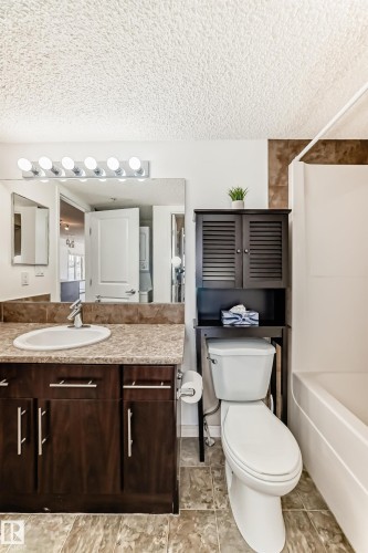 Bathroom featuring a vanity with a sink and dark wood cabinetry, a mirror with overhead lighting, a toilet, and a bathtub with tiled walls - 301 103 Ambleside Drive, Edmonton, AB - Indoor Photo Showing Bathroom