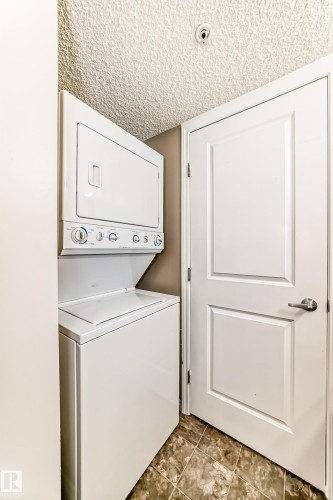 Laundry area featuring a stacked washer and dryer, a paneled door, and tiled flooring - 301 103 Ambleside Drive, Edmonton, AB - Indoor Photo Showing Laundry Room