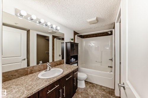 Bathroom with a vanity featuring a single sink, a large mirror, and a bathtub with an integrated shower - 301 103 Ambleside Drive, Edmonton, AB - Indoor Photo Showing Bathroom