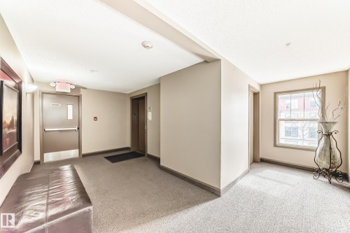 The property features a hallway with carpeted flooring, neutral-toned walls, and a window providing natural light - 301 103 Ambleside Drive, Edmonton, AB - Indoor Photo Showing Other Room