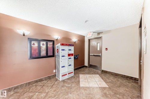 The property features a hallway with tiled flooring, a brown accent wall, and wall sconce lighting - 301 103 Ambleside Drive, Edmonton, AB - Indoor Photo Showing Other Room
