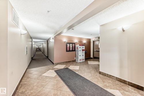 The property features a well-lit corridor with wall-mounted lighting fixtures, tile flooring, and a textured ceiling - 301 103 Ambleside Drive, Edmonton, AB - Indoor Photo Showing Other Room