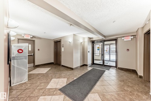 The property features a well-maintained entry area with tiled flooring, neutral wall colors, and wall sconce lighting - 301 103 Ambleside Drive, Edmonton, AB - Indoor Photo Showing Other Room